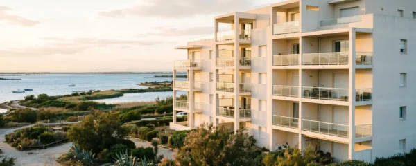 Résidence contemporaine aux façades blanches dans le quartier Coudalère à Port Leucate, avec balcons orientés sud donnant sur l'étang de Salses-Leucate en arrière-plan, végétation méditerranéenne au premier plan, lumière dorée de fin d'après-midi